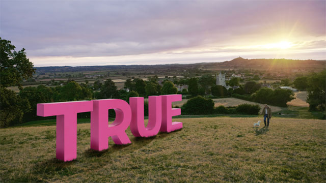 Promotional image showing the word 'TRUE' on a hilltop looking across to Glastonbury Tor